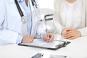 Unknown doctor and female patient discussing something while standing near reception desk in emergency hospit