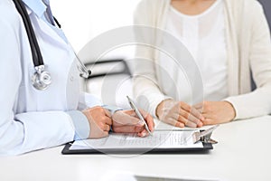 Unknown doctor and female patient discussing something while standing near reception desk in emergency hospit