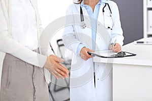 Unknown doctor and female patient discussing something while standing near reception desk in emergency hospit