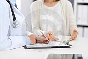 Unknown doctor and female patient discussing something while standing near reception desk in emergency hospit