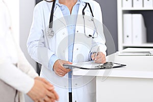 Unknown doctor and female patient discussing something while standing near reception desk in emergency hospit