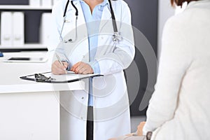 Unknown doctor and female patient discussing something while standing near reception desk in emergency hospit