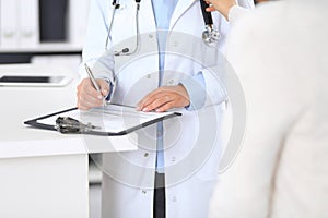 Unknown doctor and female patient discussing something while standing near reception desk in emergency hospit