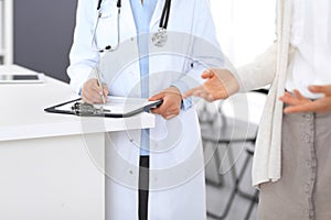 Unknown doctor and female patient discussing something while standing near reception desk in emergency hospit