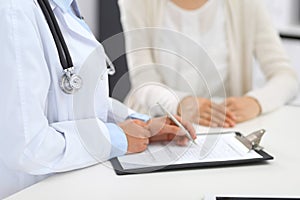 Unknown doctor and female patient discussing something while standing near reception desk in emergency hospit