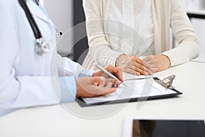 Unknown doctor and female patient discussing something while standing near reception desk in emergency hospital