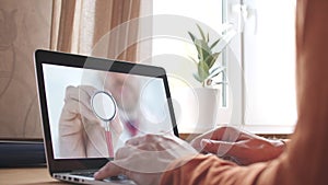 Unknown doctor holds stethoscope bell on the screen of a laptop at home. Modern telemedicine related shot