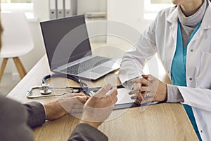 Unknown doctor and patient talk during medical consultation while sitting at table in office.