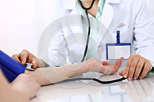 Unknown doctor woman checking blood pressure of female patient, close-up. Cardiology in medicine and health care concept