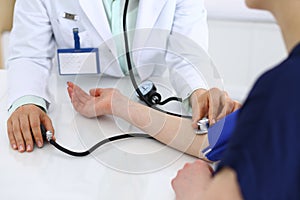 Unknown doctor woman checking blood pressure of female patient, close-up. Cardiology in medicine and health care concept