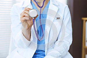 Unknown doctor woman holds stethoscope head, close-up. Physician ready to examine and help patient. Helping and