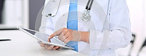 Unknown doctor woman at work. Female physician using digital tablet while standing near reception desk at clinic or