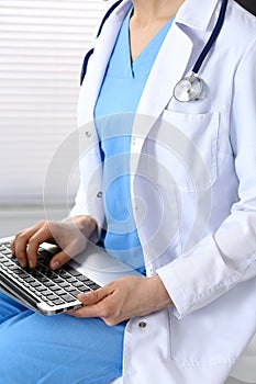 Unknown female doctor typing on laptop computer while sitting at chair in clinic. Medical staff, compulsory work concep