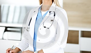 Unknown female physician is standing at her workplace near desktop computer, close-up. Medicine concept