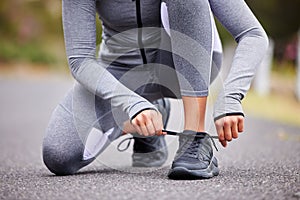 Unknown fit woman tying the laces of her sneakers for exercise outdoors. Unrecognizable athlete fixing her shoes to get