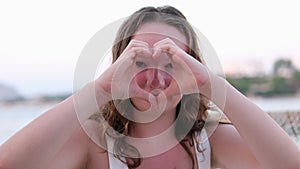 Unknown girl with the red hoody forming a heart shape with hands-on a breezy day such that the light ray passes through