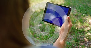 Unknown hands holding tablet on nature. Unrecognizable man have gadget on picnic