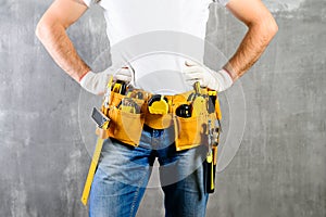 unknown handyman with hands on waist and tool belt with construction tools against grey background. DIY tools and manual work con