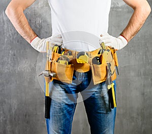 unknown handyman with hands on waist and tool belt with construction tools against grey background. DIY tools and manual work con