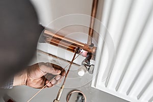 Unknown industrial worker plumber with central heating copper pipes welding using gas torch or blowtorch on the wall in house