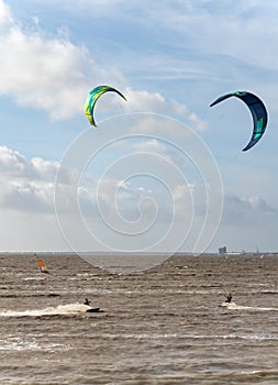 Unknown kitesurfers surf on brown water with waves from the Atlantic
