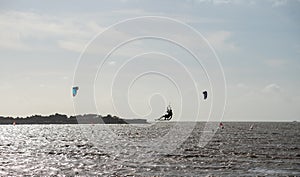 Unknown kitesurfers surf on brown water with waves from the Atlantic Ocean