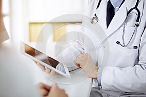 Unknown male doctor and patient woman discussing current health examination while sitting in sunny clinic and using