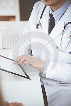 Unknown male doctor and patient woman discussing current health examination while sitting in sunny clinic and using