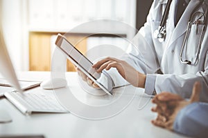 Unknown male doctor and patient woman discussing current health examination while sitting in sunny clinic and using