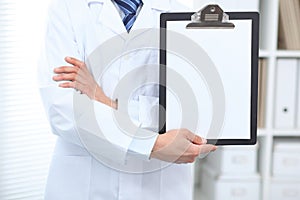 Unknown male doctor standing straight while holding medical clipboard with blank white paper. Medicine and health care