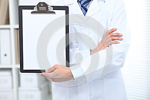 Unknown male doctor standing straight while holding medical clipboard with blank white paper. Medicine and health care