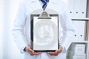 Unknown male doctor standing straight while holding medical form. Medicine and health care concept