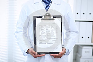 Unknown male doctor standing straight while holding medical form. Medicine and health care concept