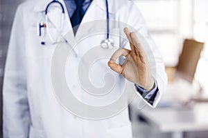 Unknown male doctor standing straight with OK sign in sunny clinic, closeup. Perfect medical service in hospital