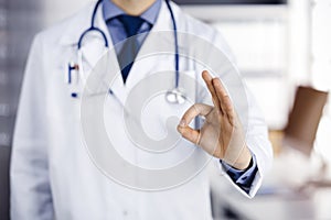 Unknown male doctor standing straight with OK sign in sunny clinic, closeup. Perfect medical service in hospital