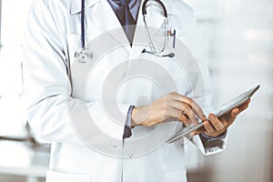 Unknown male doctor using tablet computer in clinic near his working place, closeup. Perfect medical service in hospital