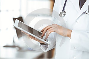 Unknown male doctor using tablet computer in clinic near his working place, closeup. Perfect medical service in hospital