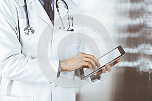 Unknown male doctor using tablet computer in clinic near his working place, closeup. Perfect medical service in hospital