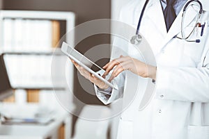 Unknown male doctor using tablet computer in clinic near his working place, closeup. Perfect medical service in hospital