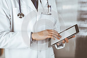 Unknown male doctor using tablet computer in clinic near his working place, closeup. Perfect medical service in hospital