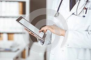 Unknown male doctor using tablet computer in clinic near his working place, closeup. Perfect medical service in hospital