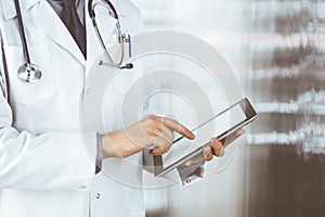 Unknown male doctor using tablet computer in clinic near his working place, closeup. Perfect medical service in hospital