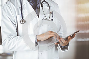 Unknown male doctor using tablet computer in sunny clinic, closeup. Perfect medical service in hospital. Medicine and