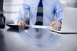 Unknown man accountant in blue shirt use calculator and computer with holding pen on while staying at home during covid