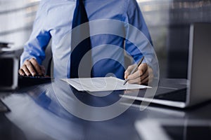 Unknown man accountant in blue shirt use calculator and computer with holding pen on while staying at home during covid