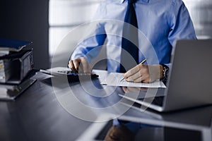 Unknown man accountant in blue shirt use calculator and computer with holding pen on while staying at home during covid