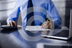 Unknown man accountant in blue shirt use calculator and computer with holding pen on while staying at home during covid