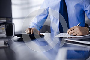 Unknown man accountant in blue shirt use calculator and computer with holding pen on while staying at home during covid