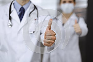 Unknown man-doctor and woman standing straight as a team and showing Ok sign with thumbs up in modern clinic. Medicine
