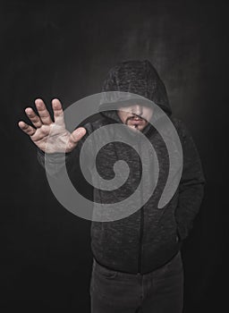 Unknown man in hood pointing by hand on dark. Focus on hand